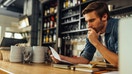 A small business owner reviews financial documents while standing behind a counter.